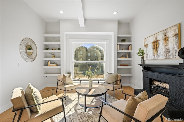 living area with beam ceiling, built in features, light wood-type flooring, and a fireplace