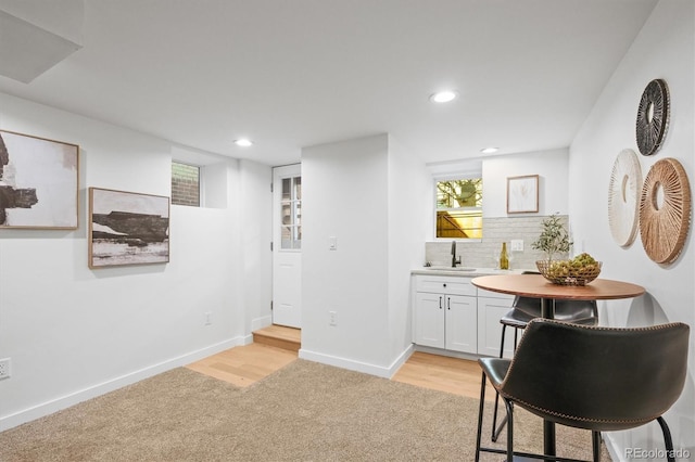 bar featuring light carpet, backsplash, sink, and white cabinetry