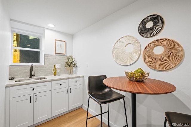 kitchen with white cabinets, sink, backsplash, light stone counters, and light hardwood / wood-style flooring