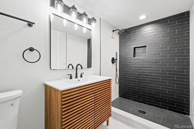 bathroom featuring toilet, vanity, tiled shower, and tile patterned flooring