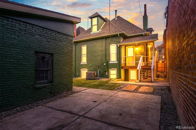 back house at dusk featuring cooling unit and a patio