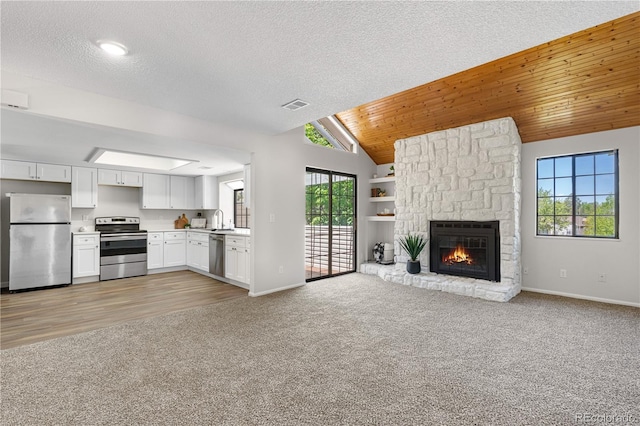 unfurnished living room featuring light colored carpet, baseboards, a fireplace, vaulted ceiling, and a sink