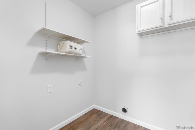 laundry room featuring electric dryer hookup, baseboards, dark wood-type flooring, and cabinet space