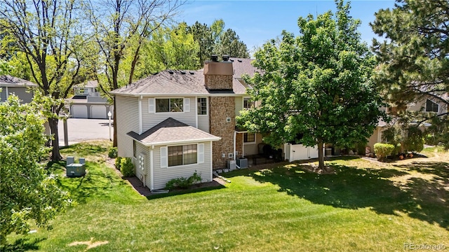 back of property featuring an outdoor structure, a chimney, a lawn, central AC unit, and a shingled roof