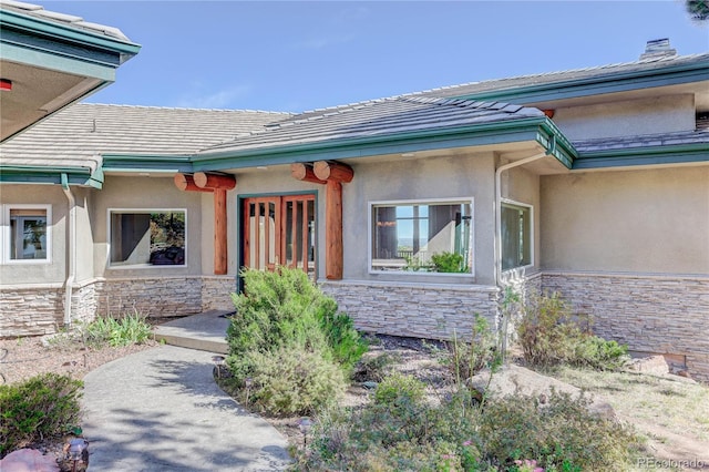 entrance to property featuring a tiled roof, stone siding, and stucco siding