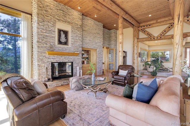 living area with beam ceiling, wood finished floors, a high ceiling, a stone fireplace, and wood ceiling