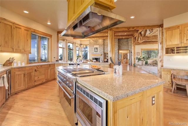 kitchen featuring light wood finished floors, stainless steel microwave, a kitchen island, a large fireplace, and range