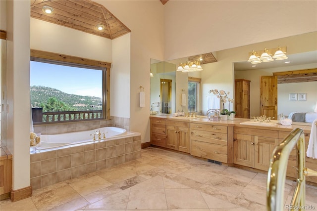 full bathroom featuring baseboards, a garden tub, double vanity, a towering ceiling, and a sink