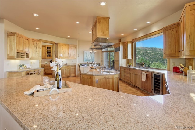 4440 Monitor Rock Ln, Colorado Springs, CO 80904 - kitchen featuring beverage cooler, an island with sink, light stone counters, recessed lighting, and ventilation hood