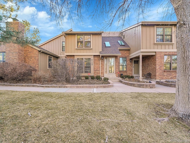 view of front of property with a shingled roof, a front yard, and brick siding