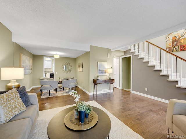 living room with visible vents, baseboards, wood finished floors, stairs, and a textured ceiling