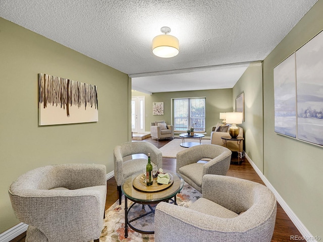 living area featuring a textured ceiling, baseboards, and wood finished floors