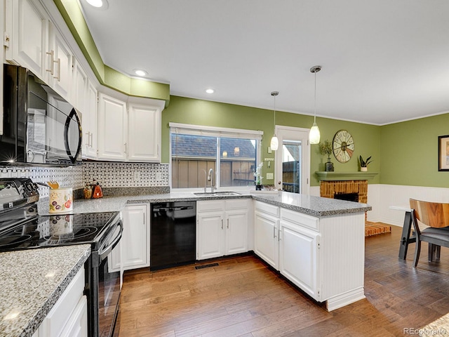 kitchen featuring a peninsula, wood finished floors, a sink, white cabinets, and black appliances