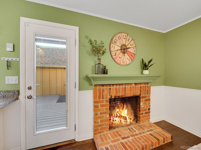 doorway featuring a wainscoted wall, ornamental molding, a fireplace, and wood finished floors