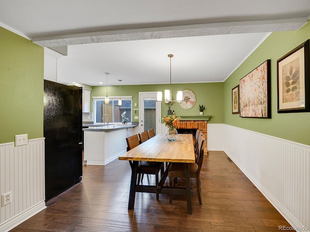 dining area featuring a wainscoted wall, a fireplace, dark wood finished floors, and a chandelier