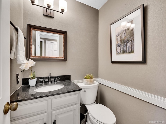 bathroom with toilet, a textured wall, and vanity