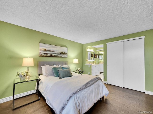 bedroom with a textured ceiling, connected bathroom, wood finished floors, baseboards, and a closet