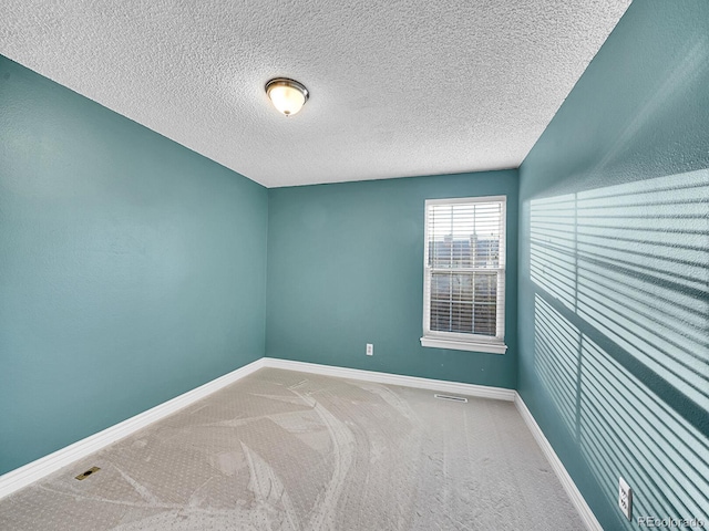 empty room with carpet floors, visible vents, a textured ceiling, and baseboards