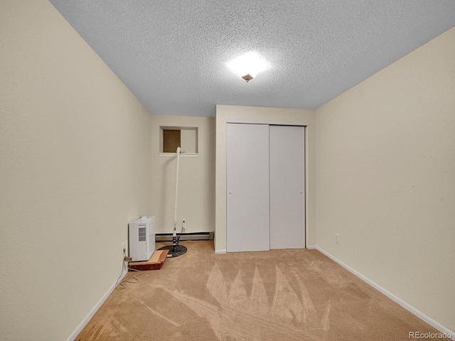 unfurnished bedroom featuring baseboards, a textured ceiling, carpet floors, a baseboard heating unit, and a closet