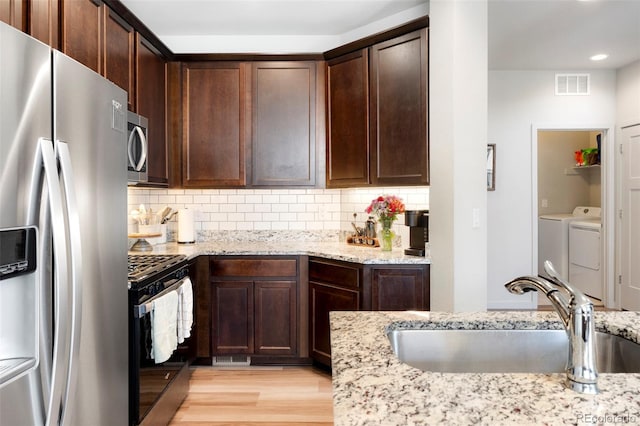 kitchen featuring appliances with stainless steel finishes, a sink, dark brown cabinets, light wood-type flooring, and light stone countertops