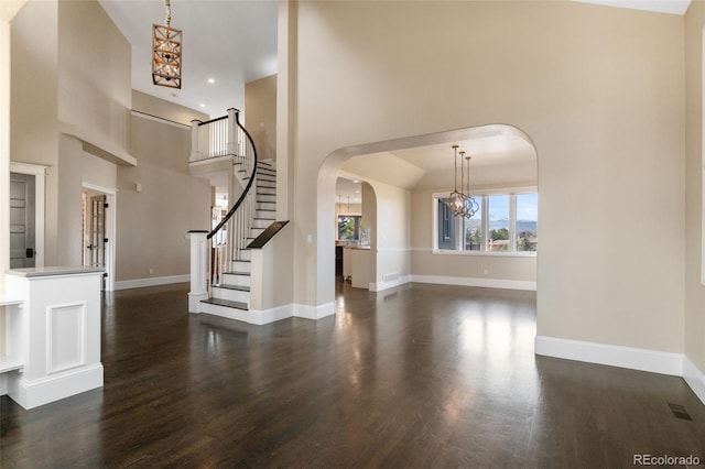 interior space with dark wood-type flooring, a towering ceiling, and a chandelier