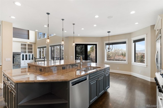 kitchen featuring sink, light stone counters, decorative light fixtures, stainless steel dishwasher, and a large island with sink