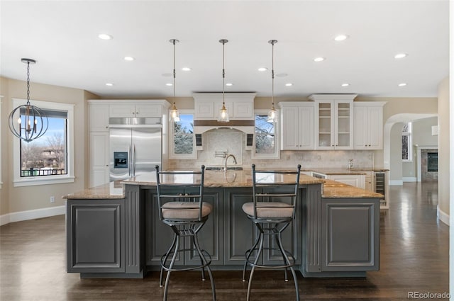 kitchen featuring white cabinets, stainless steel built in refrigerator, hanging light fixtures, and a large island with sink