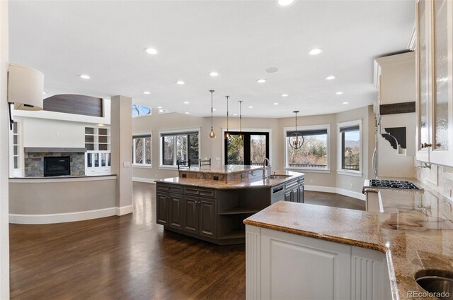 kitchen featuring hanging light fixtures, light stone counters, a fireplace, a center island with sink, and dark hardwood / wood-style flooring