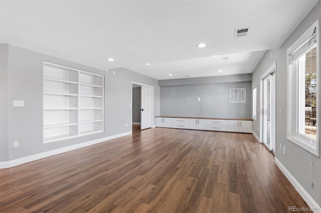 unfurnished living room featuring dark hardwood / wood-style floors and built in shelves