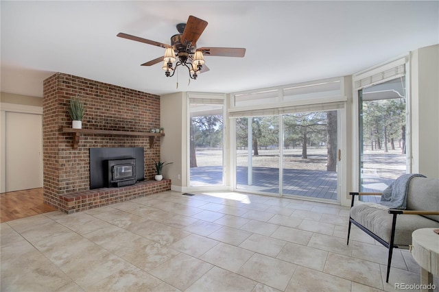 unfurnished living room with a wood stove, ceiling fan, light tile patterned flooring, and a healthy amount of sunlight