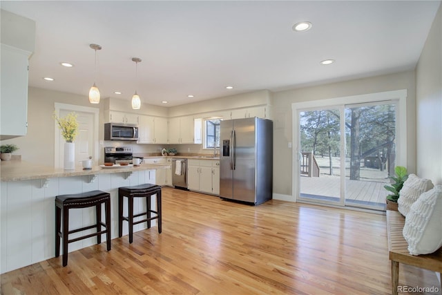 kitchen with kitchen peninsula, pendant lighting, stainless steel appliances, and white cabinetry