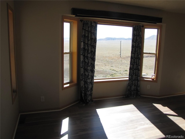 spare room with a mountain view, plenty of natural light, and dark hardwood / wood-style floors