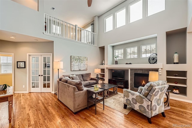 living room with a tiled fireplace, light hardwood / wood-style flooring, french doors, and a healthy amount of sunlight