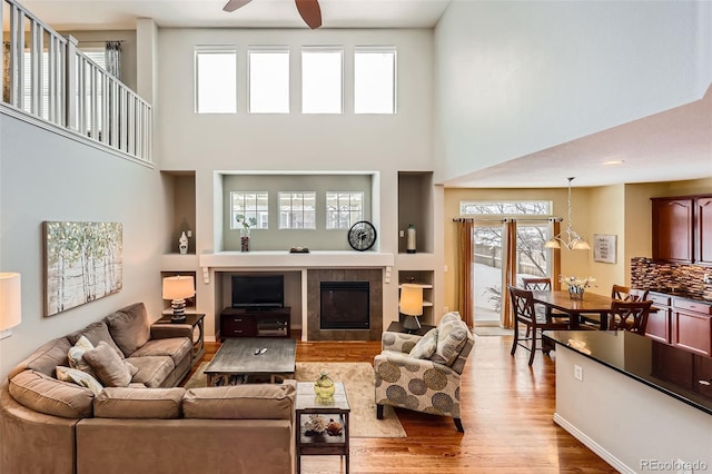 living room with ceiling fan, a tiled fireplace, light hardwood / wood-style floors, and a high ceiling