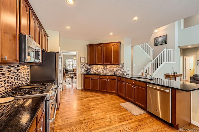 kitchen featuring sink, appliances with stainless steel finishes, backsplash, dark stone counters, and light wood-type flooring