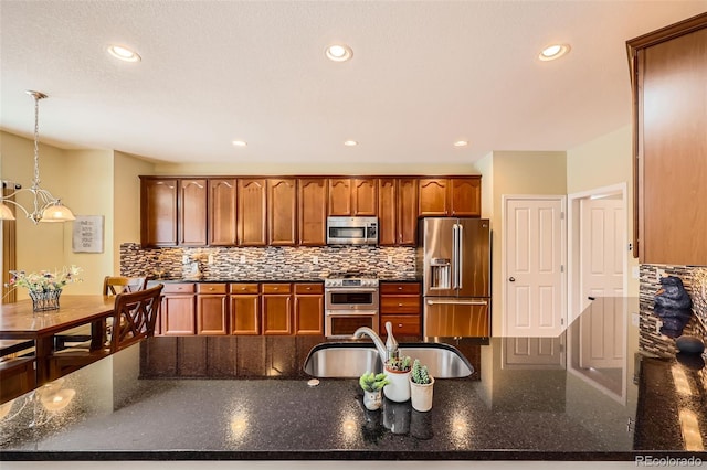 kitchen featuring appliances with stainless steel finishes, pendant lighting, sink, dark stone countertops, and backsplash