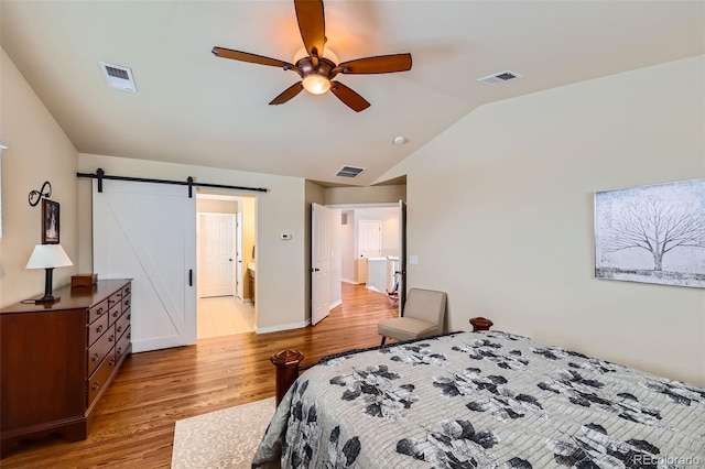 bedroom with ceiling fan, lofted ceiling, a barn door, and light wood-type flooring