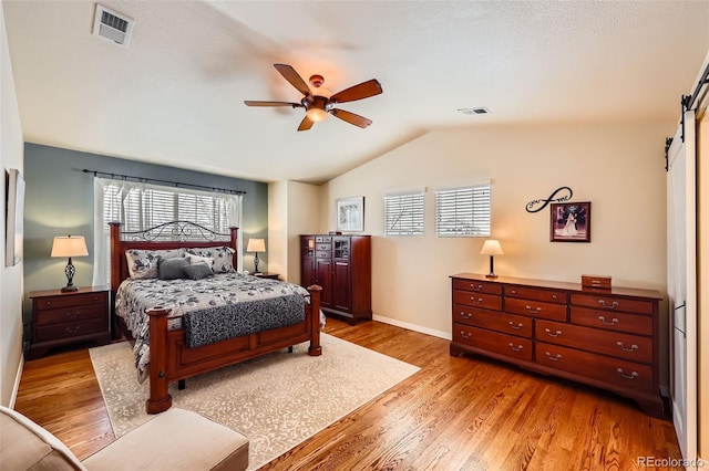 bedroom with vaulted ceiling, light wood-type flooring, ceiling fan, a barn door, and a textured ceiling