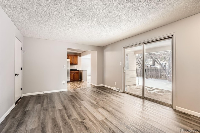 unfurnished living room featuring baseboards, a textured ceiling, visible vents, and wood finished floors