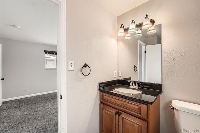 half bath featuring a textured wall, toilet, vanity, and baseboards