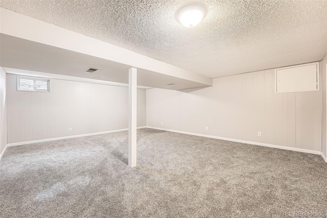 basement with carpet floors, visible vents, a textured ceiling, and baseboards