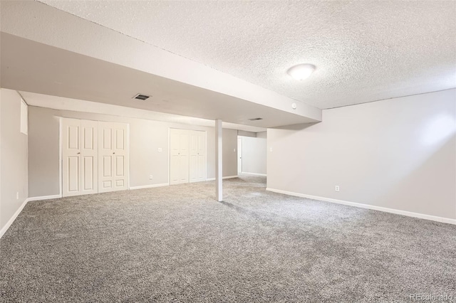 finished basement with carpet, a textured ceiling, visible vents, and baseboards