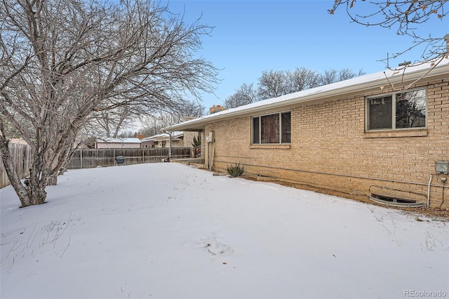 view of snowy exterior with brick siding and fence