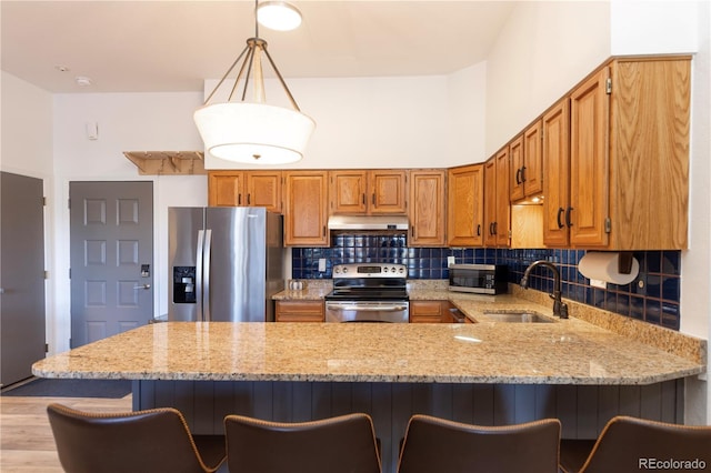 kitchen featuring a sink, under cabinet range hood, stainless steel appliances, a peninsula, and decorative backsplash