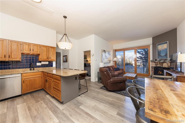 kitchen with light wood-style flooring, a sink, a stone fireplace, dishwasher, and open floor plan