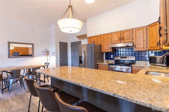 kitchen featuring under cabinet range hood, backsplash, stainless steel appliances, and a breakfast bar