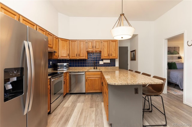 kitchen featuring a peninsula, a sink, appliances with stainless steel finishes, a kitchen bar, and tasteful backsplash