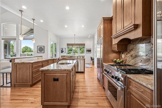 13962 W 76th Ln, Arvada, CO 80005 - kitchen featuring a center island with sink, appliances with stainless steel finishes, light wood-style flooring, brown cabinets, and recessed lighting