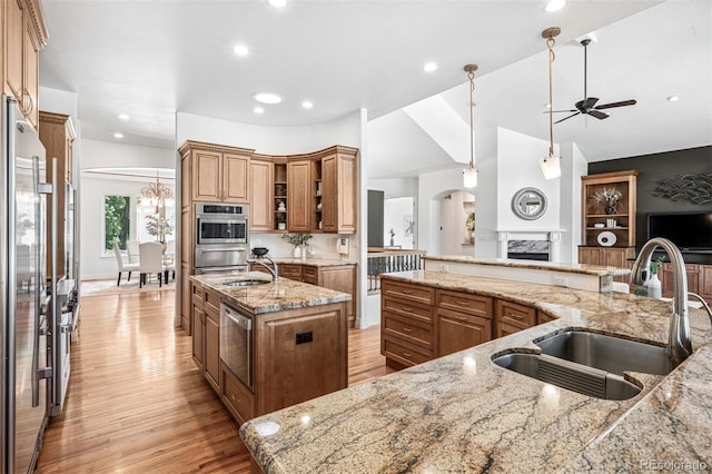 13962 W 76th Ln, Arvada, CO 80005 - kitchen featuring ceiling fan, a large island, light wood finished floors, appliances with stainless steel finishes, and a high end fireplace