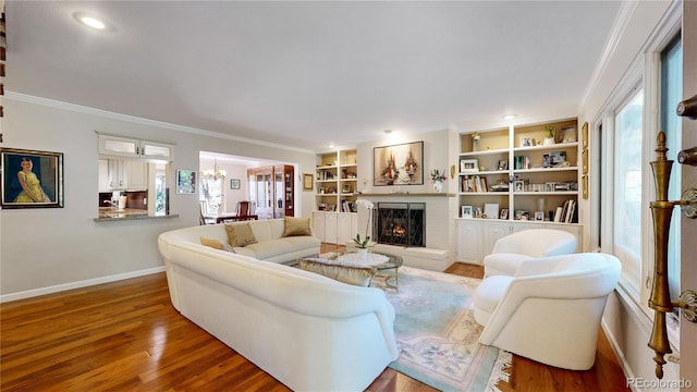 living room featuring built in features, a brick fireplace, hardwood / wood-style flooring, a notable chandelier, and crown molding